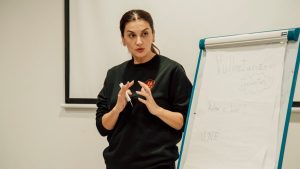 Woman confidently presenting with a flip chart in a classroom setting.